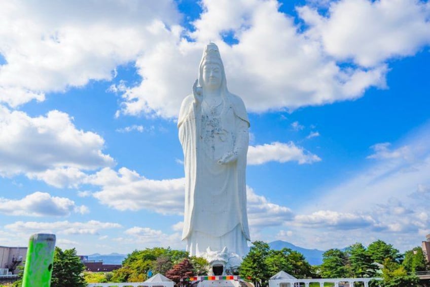 A large white statue of a figure with a halo, set against a blue sky with clouds. 3