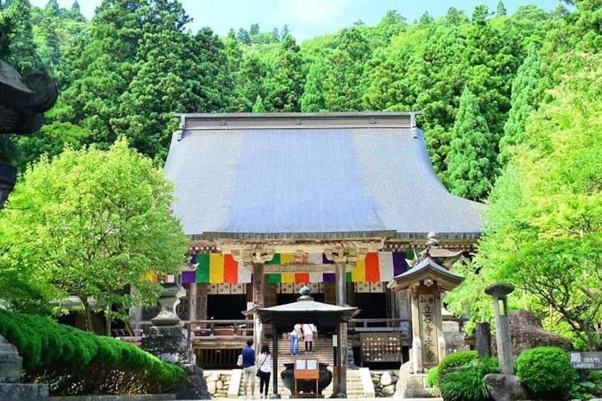 A traditional Japanese building with a sloped roof, surrounded by lush greenery and stone lanterns. 2