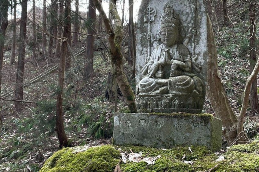 A stone statue of a seated figure in a forest. 5