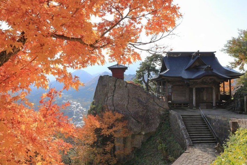 A traditional Japanese building with a steep stone staircase leading up to it, surrounded by autumn foliage. 1