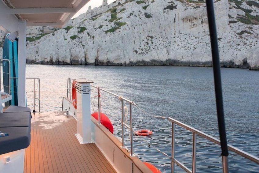 A boat deck with a railing, a lifebuoy, and a rocky coastline in the background. 3