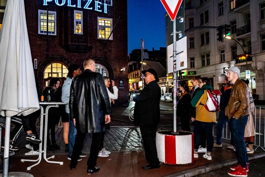 A group of people standing on a city street at night, with a police station in the background. 4