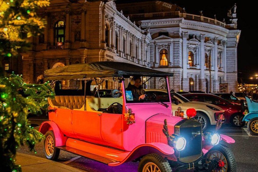 A vintage car with a pink body parked in front of a grand building. 3