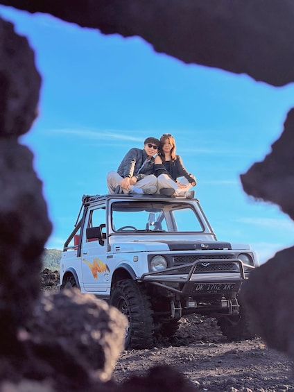 Two people sitting on a white off-road vehicle with a yellow star design, parked on a rocky terrain. 5