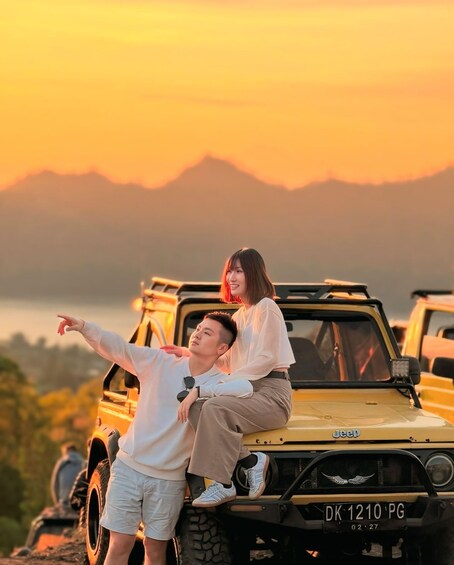 A man and a woman on a yellow off-road vehicle with a license plate 'DK 1210 PG' at sunset with mountains in the background. 4