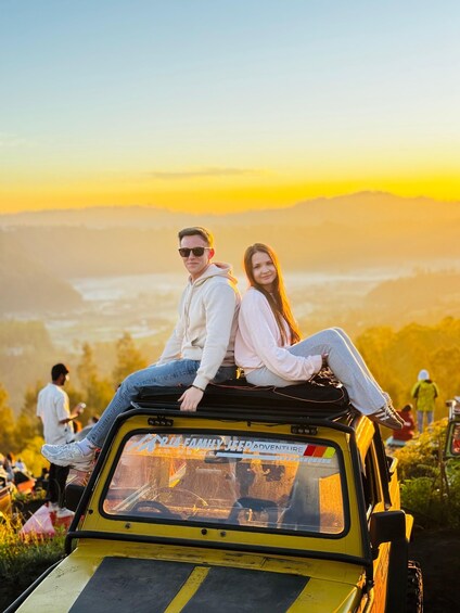 A couple sitting on the roof of a yellow vehicle with a scenic view in the background. 2