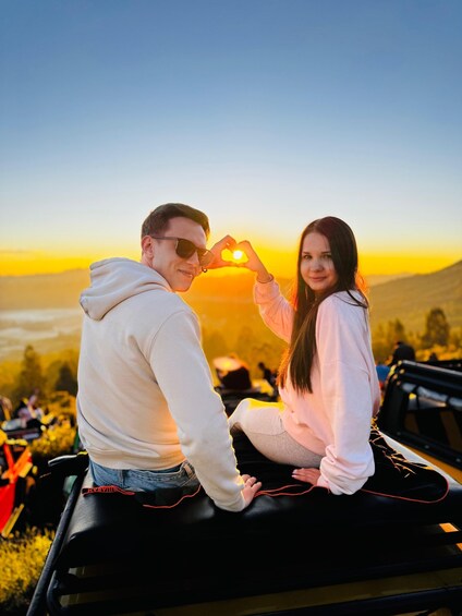 Two people sitting on a vehicle with a sunset in the background. 1