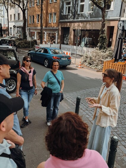 A group of people standing on a city street with buildings and parked cars in the background. 2