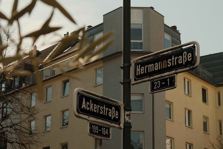 Street signs for Ackerstraße and Hermannstraße with apartment buildings in the background. 1