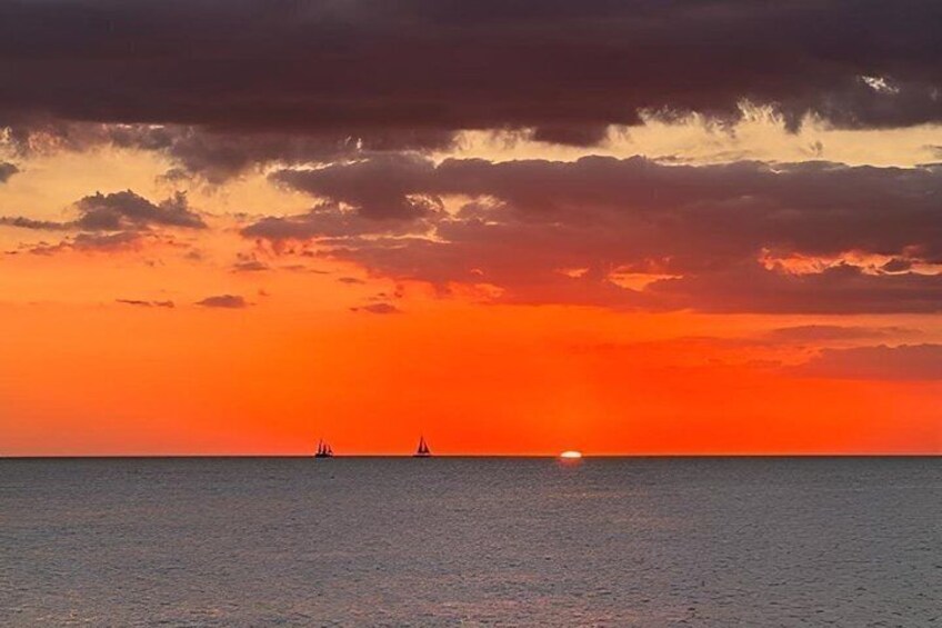 A sunset over the ocean with two sailboats. 3