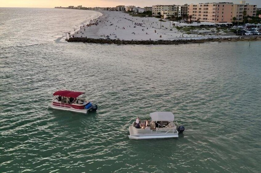 Two boats on calm water with a sandy beach and buildings in the background. 2