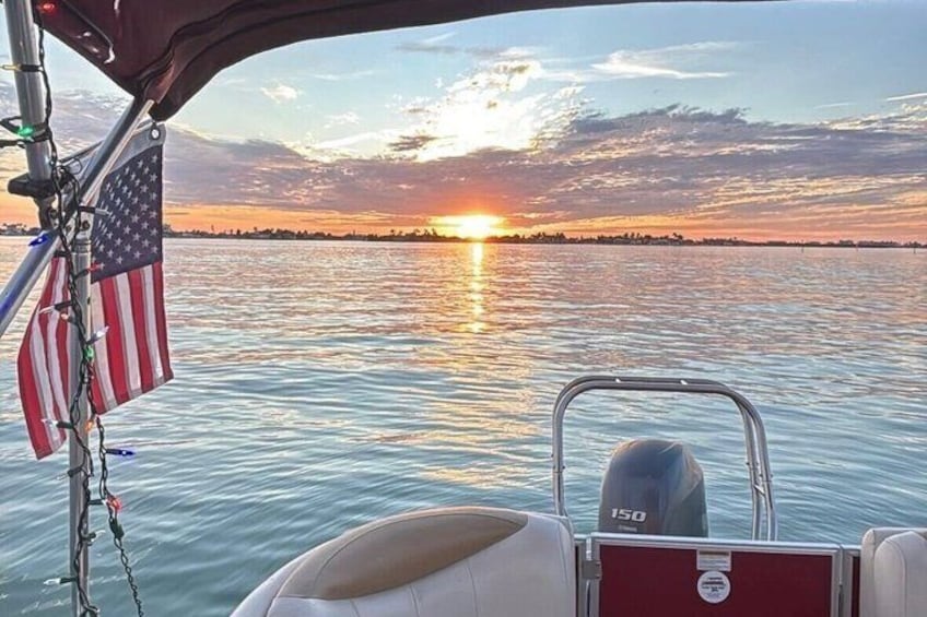 A boat with an American flag, a motor, and a sunset over water. 1