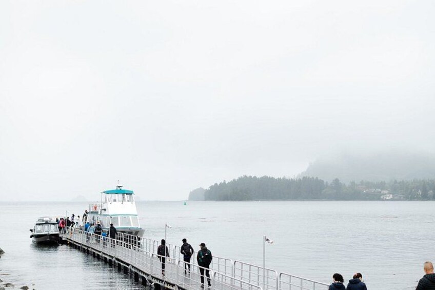 A foggy waterfront with a boat docked, people walking on a pier, and a mist-covered island in the background. 3