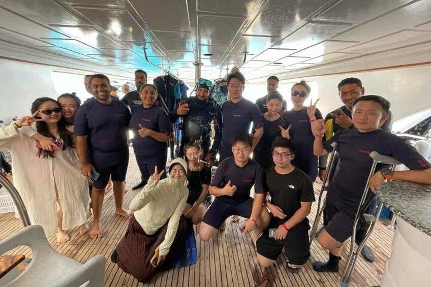 A group of people on a boat deck with a steering wheel, life jackets, and a railing. 2