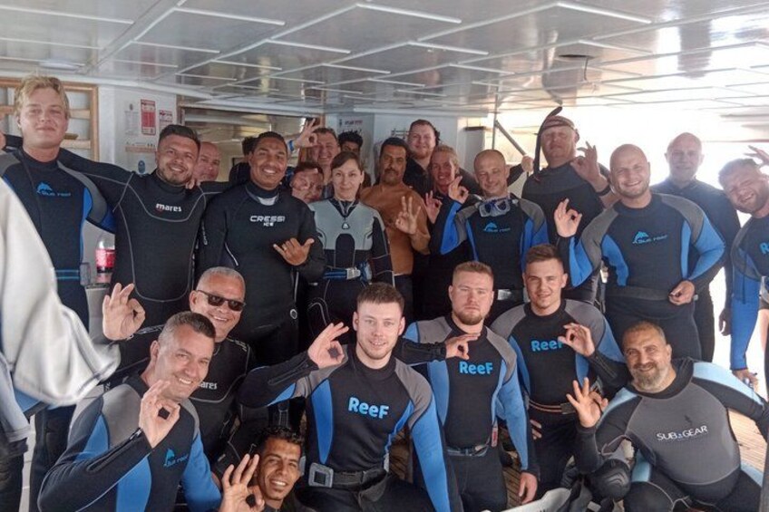 A group of people in wetsuits with 'Reef' written on them, posing for a photo in a boat. 1