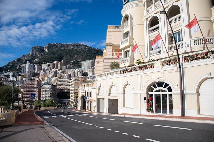 A street with a building featuring arched windows and balconies, flags, and a mountainous backdrop. 2