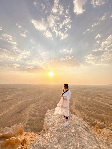 A person standing on a rocky outcrop with a vast desert landscape and a sunset in the background. 2
