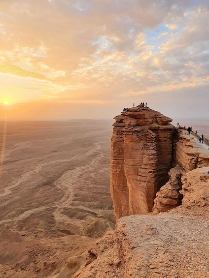A rock formation with people standing on top, overlooking a vast desert landscape. 1