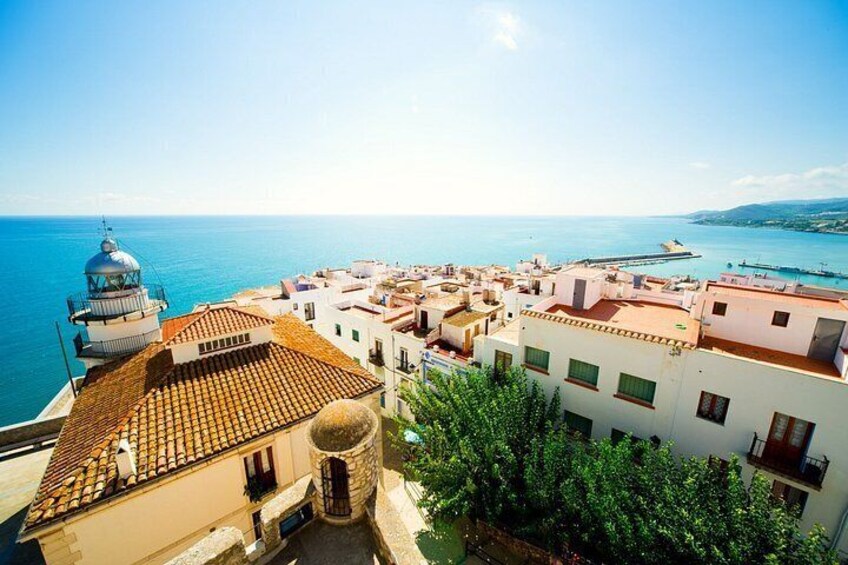 A coastal town with terracotta-roof buildings, a lighthouse, and a clear blue sea. 3