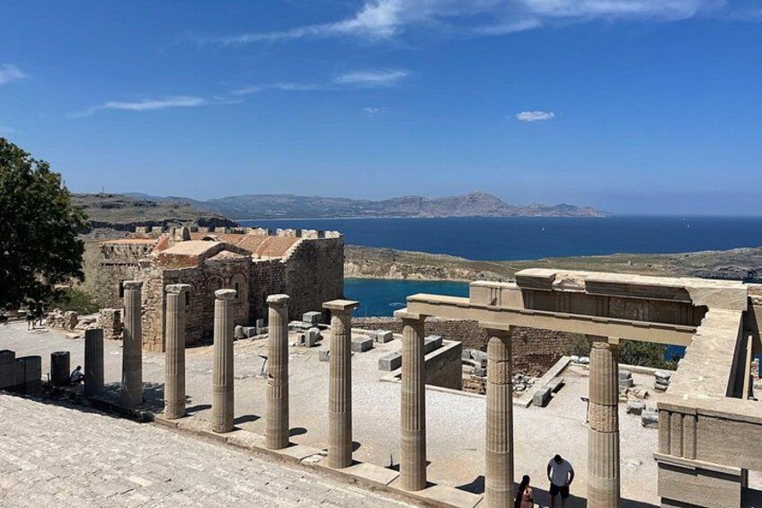 Rovine antiche con colonne, una struttura in pietra e vista sul mare e sulle montagne in lontananza. 2