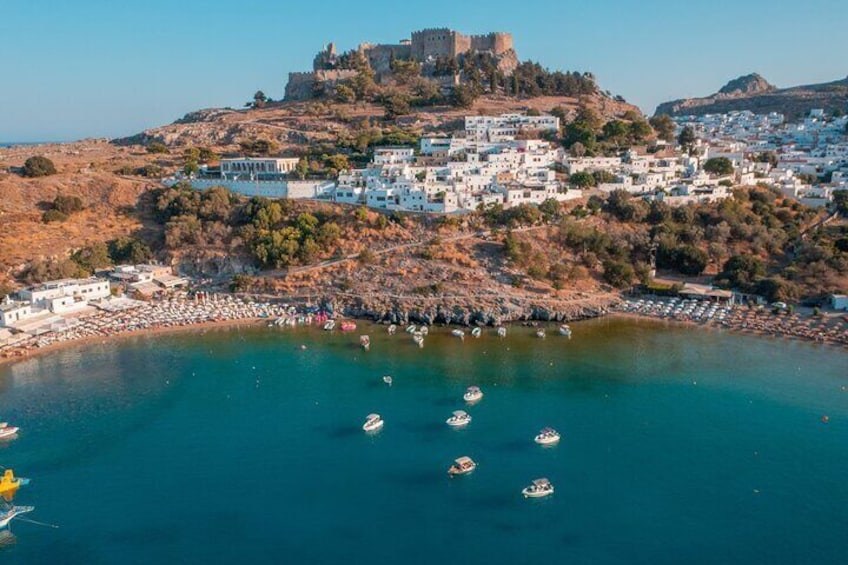 En kuststad med ett slott på en kulle, båtar på vattnet och vita byggnader. 5