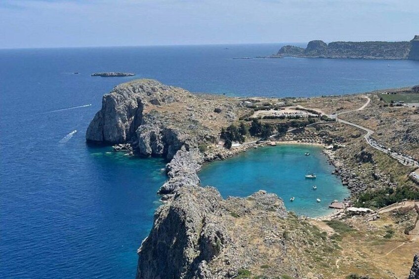 Paesaggio costiero con una baia rocciosa, acque blu cristalline e una strada tortuosa. 4
