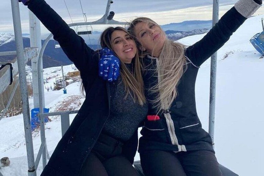 Deux personnes dans un télésiège, avec des montagnes enneigées en arrière-plan. 1