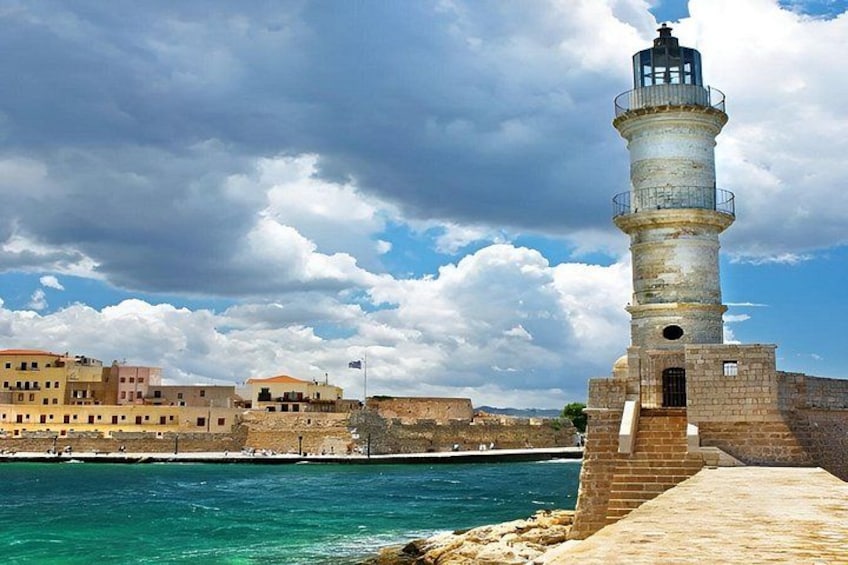 A coastal town with a prominent lighthouse, a clear blue sea, and historic buildings. 2