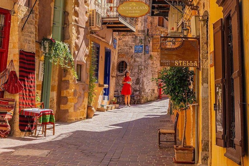 A narrow street with stone buildings, a woman in a red dress, and signs for 'ANTICA CASA STUDIOS' and 'STELLA.' 4
