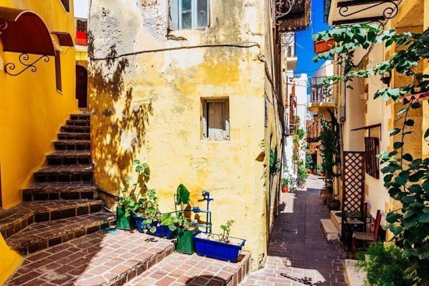 A narrow alley with yellow buildings, a staircase, and potted plants. 3