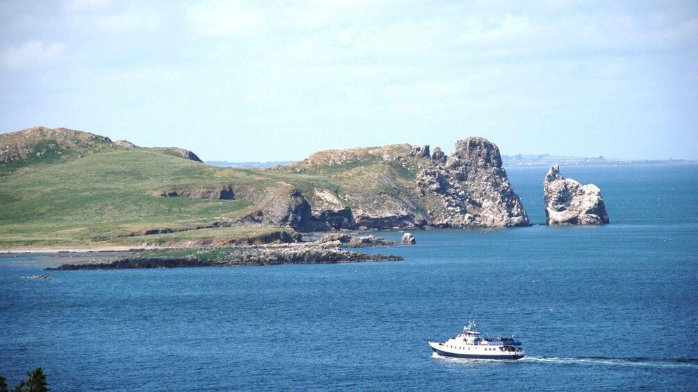 A boat on a calm sea with rocky cliffs and green hills in the background. 4