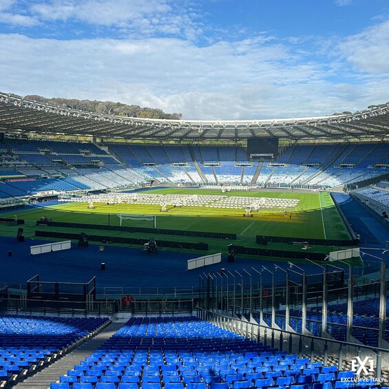 A large stadium with blue seats and a green field, under a clear sky. 1