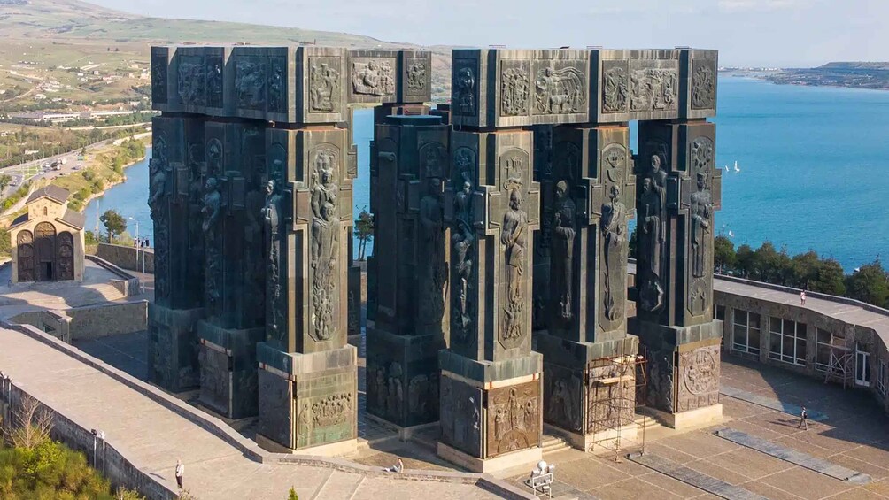Un monumento grande con esculturas en bajo relieve detalladas, cerca de un cuerpo de agua e iglesia. 3
