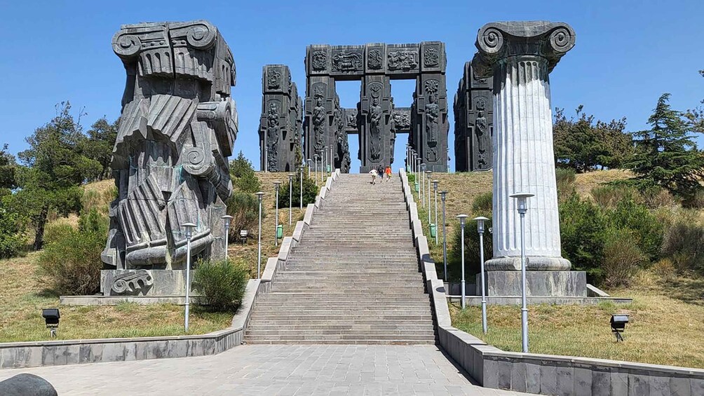 Una escalera de piedra conduce a una gran estructura de piedra con intrincados grabados, rodeada de follaje. 4