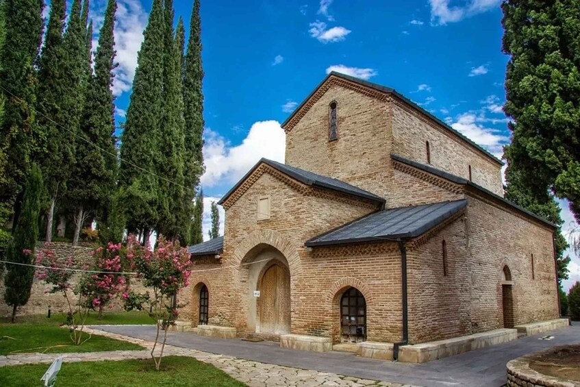 Una iglesia de ladrillo con ventanas de arco apuntado y un campanario, rodeada de árboles y un cielo despejado. 2