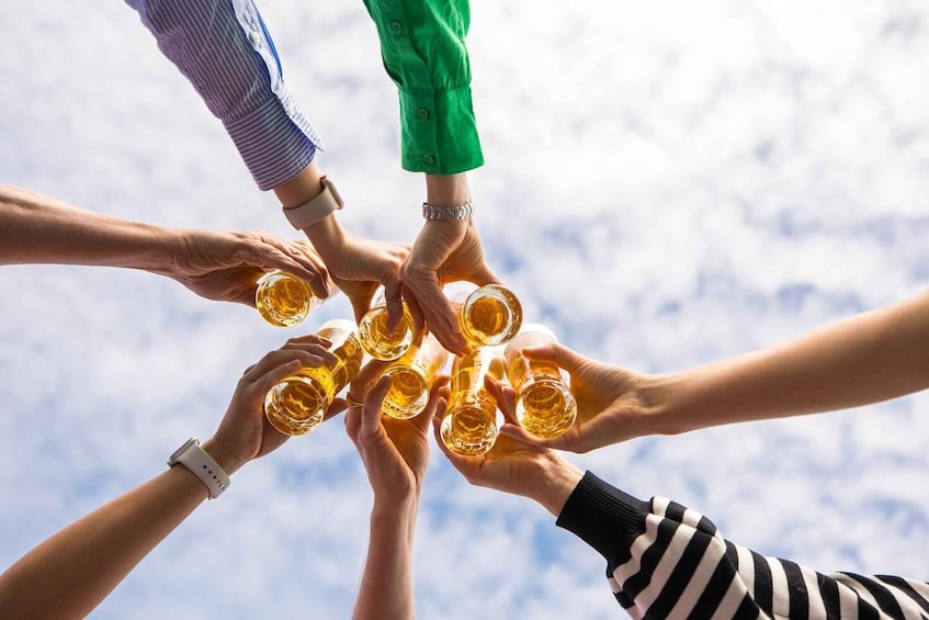 A group of people holding glasses of amber liquid, possibly beer, in a circle. 4