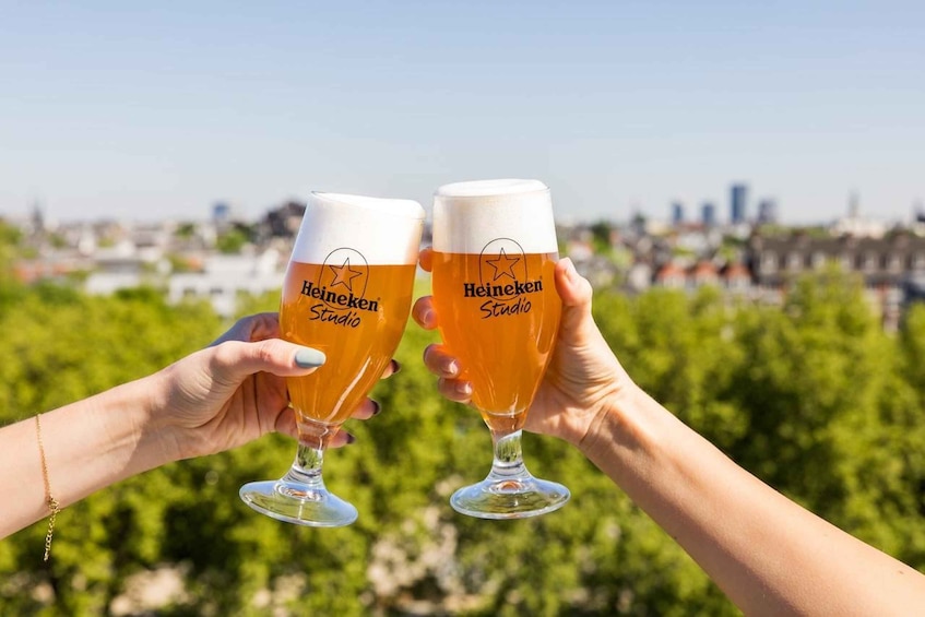 Two people holding Heineken glasses with a cityscape in the background. 1