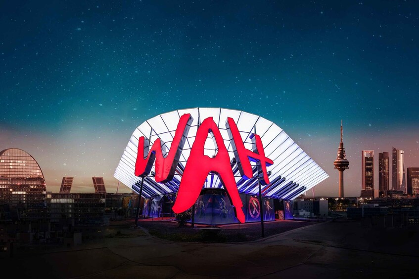 A large illuminated 'W' structure at night with a city skyline in the background. 1