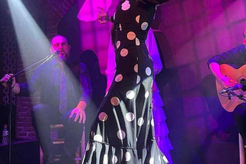 A person in a polka dot dress performing on stage with a microphone and a guitar. 4