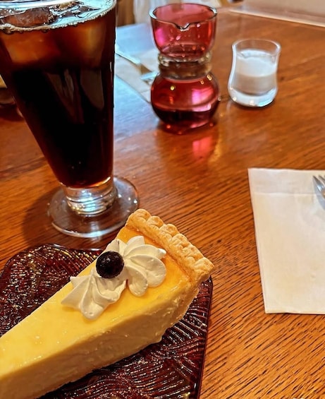 A slice of pie with a cherry on top, a glass of iced tea, and a small shot glass on a wooden table. 3