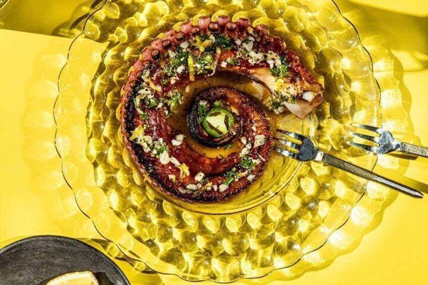 A spiral-shaped dish of octopus with lemon slices and herbs on a yellow plate. 1