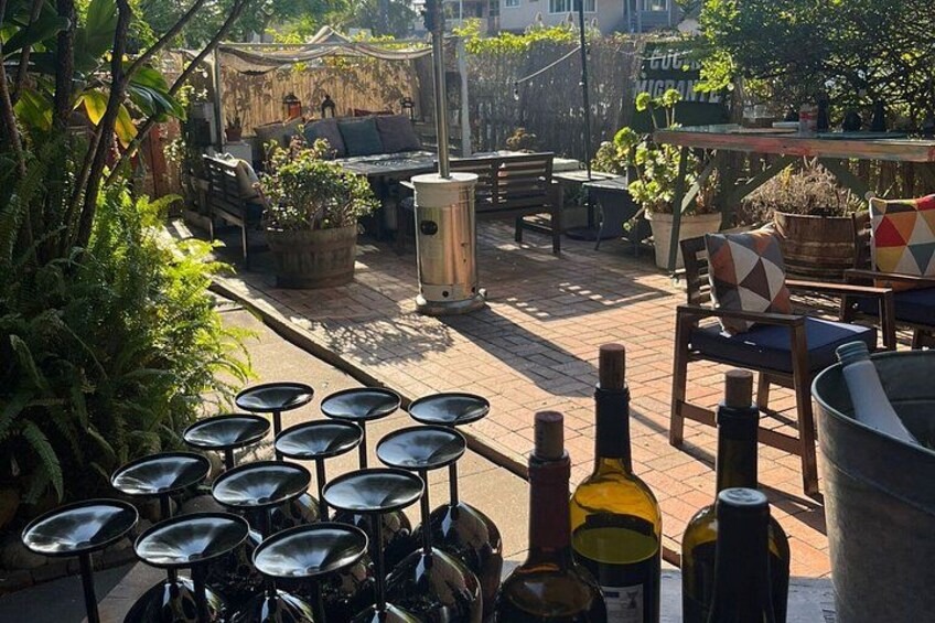 Een terras met buitenmeubels, plantenpotten en flessen wijn. 4