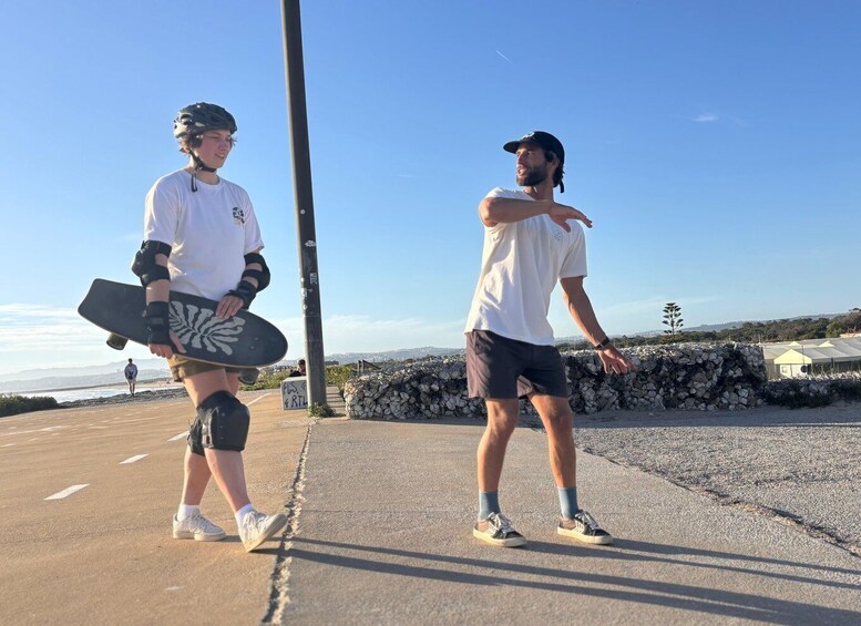 Two people skateboarding on a paved path with a clear sky and a distant view of the ocean. 4