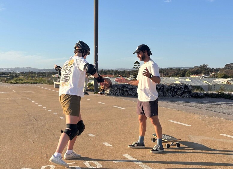 Two people skateboarding on a paved area with a clear sky and distant hills. 5