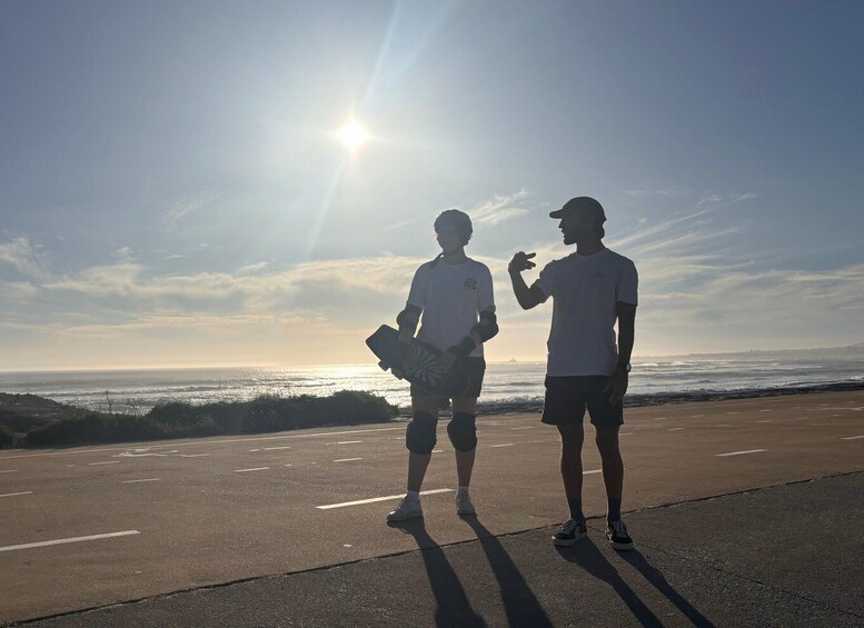 Two people standing on a road with the ocean in the background. 3