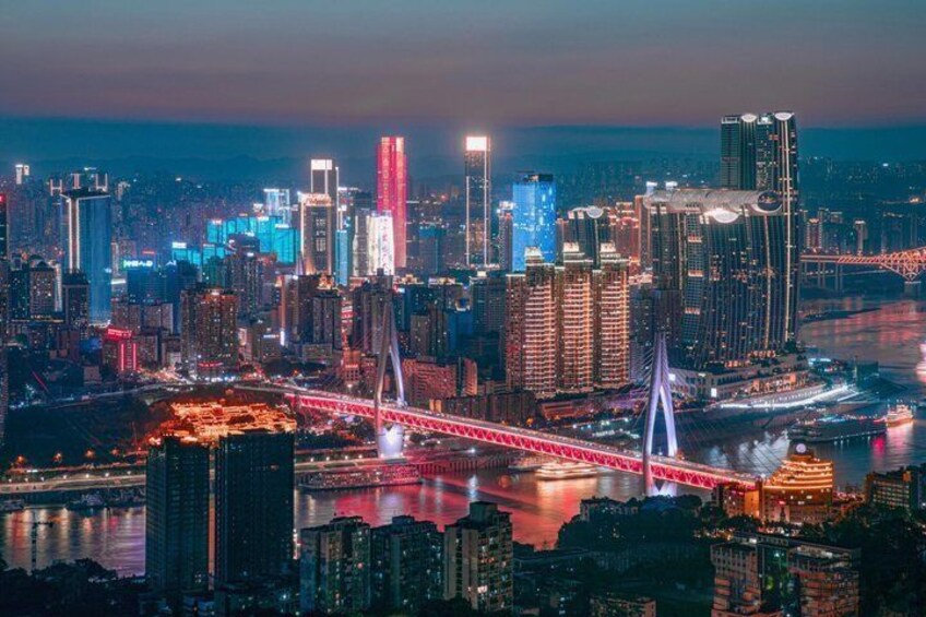 Paesaggio urbano notturno con grattacieli illuminati, un ponte rosso ben visibile e un fiume che riflette le luci della città. 1