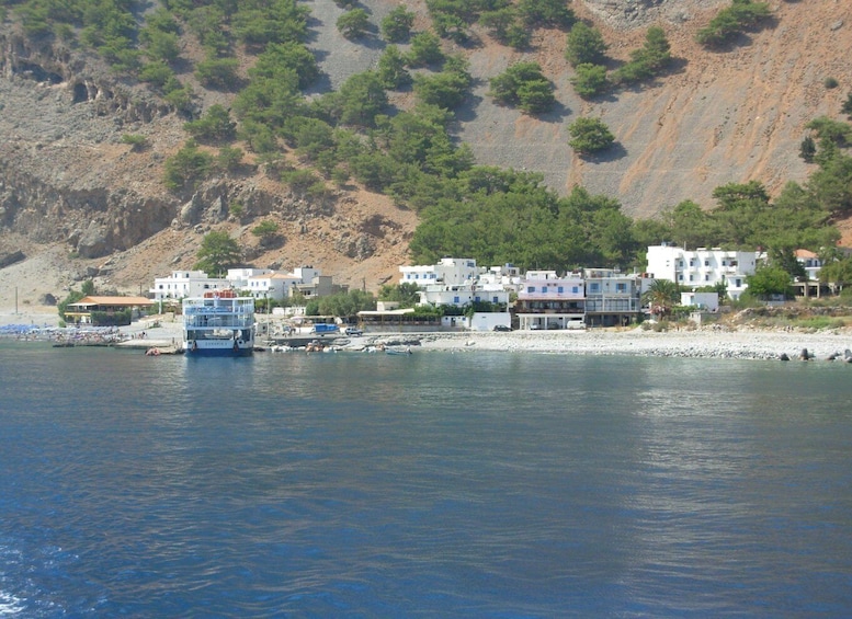 A coastal town with buildings, a ferry, and a rocky hillside. 3