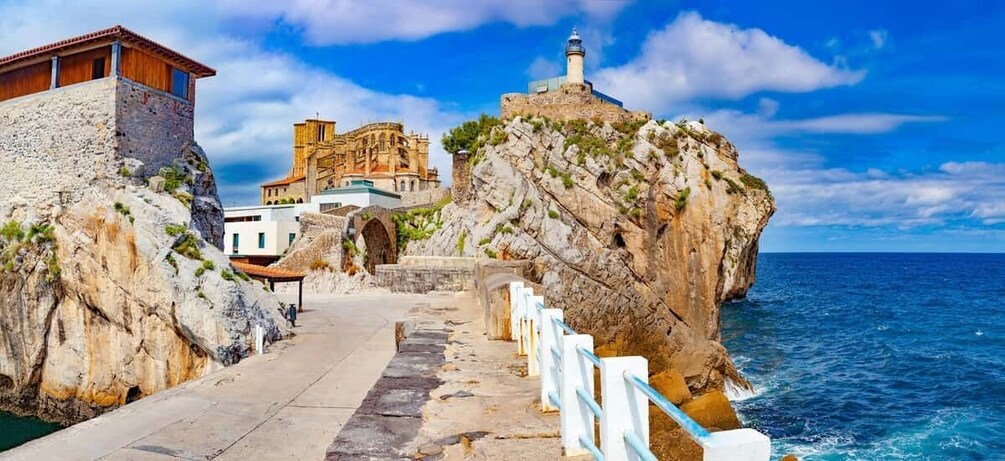 A coastal walkway with a lighthouse, historic buildings, and rocky cliffs. 2