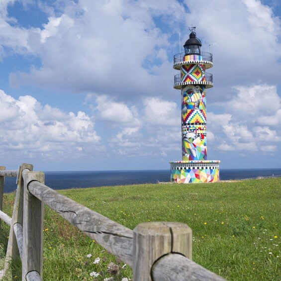 A colorful lighthouse with a weather vane on top, set against a backdrop of a clear sky and the ocean. 5