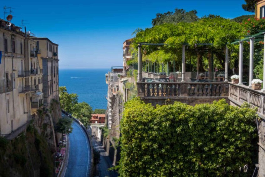 A coastal cityscape with a narrow street flanked by buildings, a clear blue sky, and the sea in the distance. 4